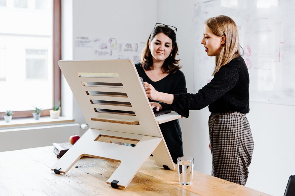 two women improve posture to look taller by working at a standing desk with laptop stand