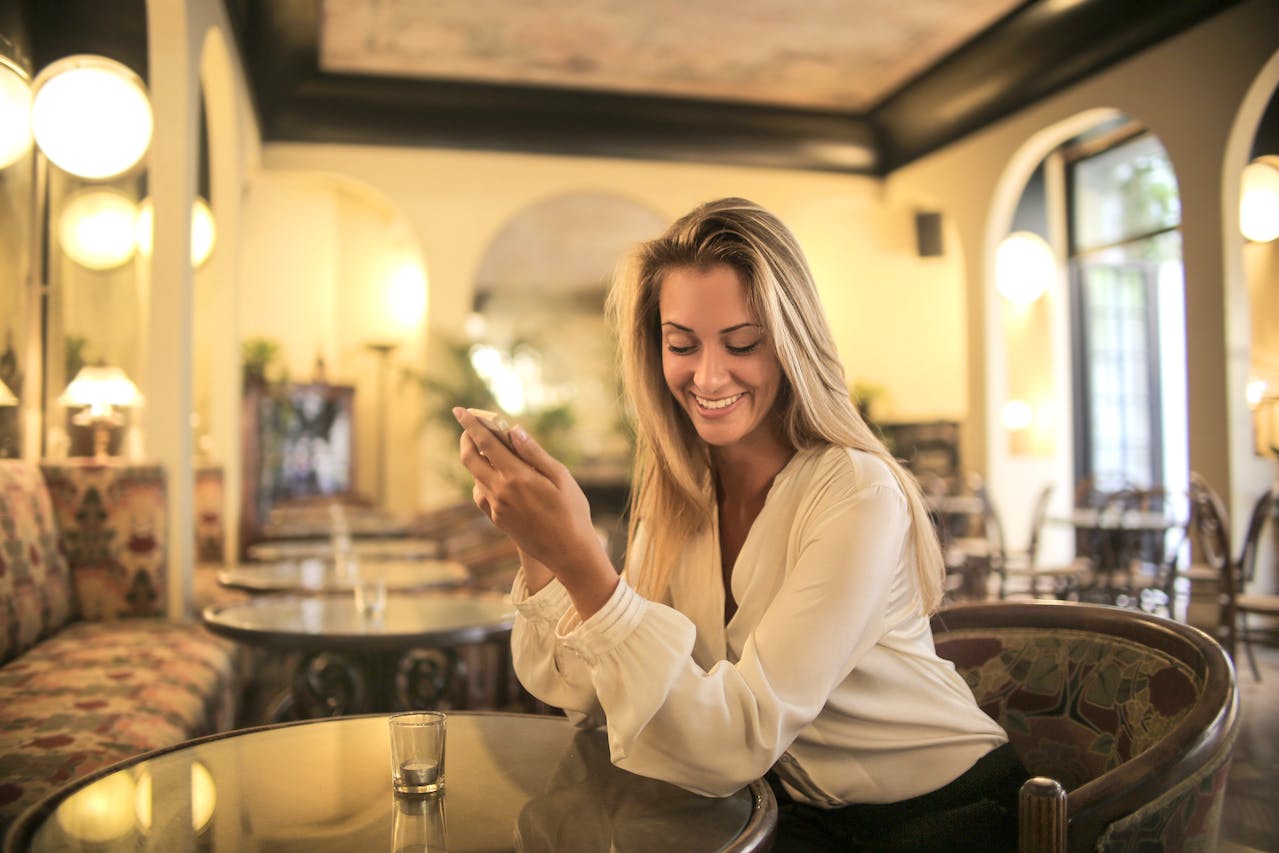 A white woman in corporate attire sitting upright in a bar after work demonstrating correct posture to use phone