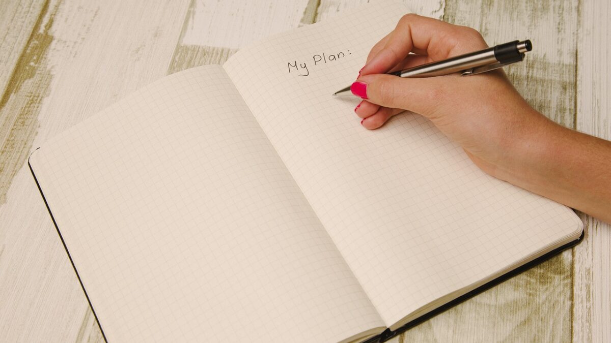 A hand and pen writing in a diary - the title "my plan" is written, planning to achieve fitness goals.