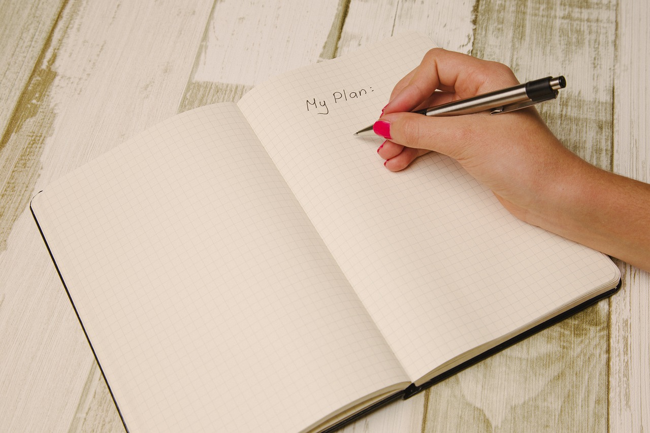 A hand and pen writing in a diary - the title "my plan" is written, planning to achieve fitness goals.