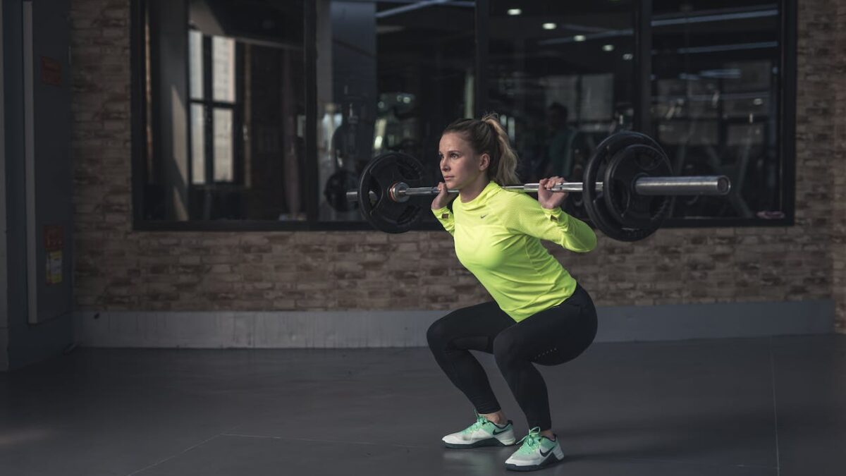 A woman in a green sports top doing back squats with a barbell, being consistent with her fitness goal ideas for beginners