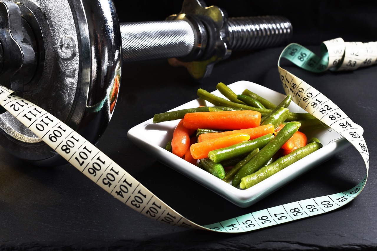 A photo of a dumbbell, some mixed vegetables, and a tape measure, highlighting the different factors when choosing an online personal trainer for weight loss