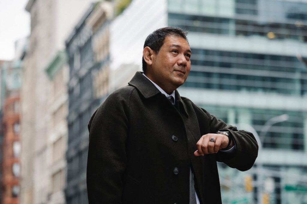 A businessman outside in the city checking his watch, appearing to be running late. Thankfully, his online personal trainer benefits means he can reschedule his planned workout easily