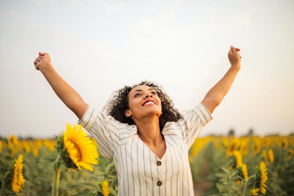 A black woman celebrating in a field of sunflowers, symbolising positive choices made in her lifestyle change journey