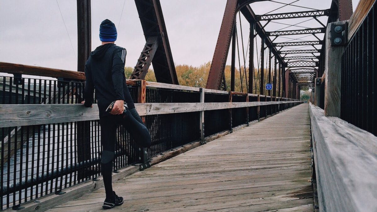 A lone man in running clothing stretching on a bridge, symbolising his healthier lifestyle change journey ahead.