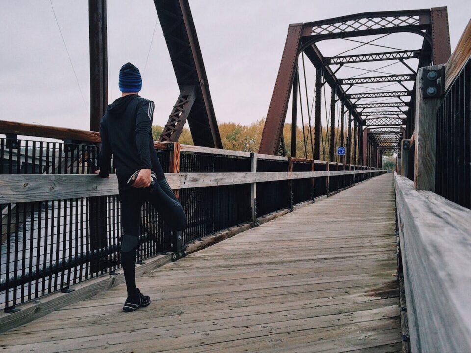 A lone man in running clothing stretching on a bridge, symbolising his healthier lifestyle change journey ahead.