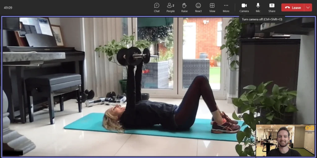 A screenshot of a video call where a client is performing a chest press exercise and has hire a personal trainer to work with her for motivation, knowledege, and accountability