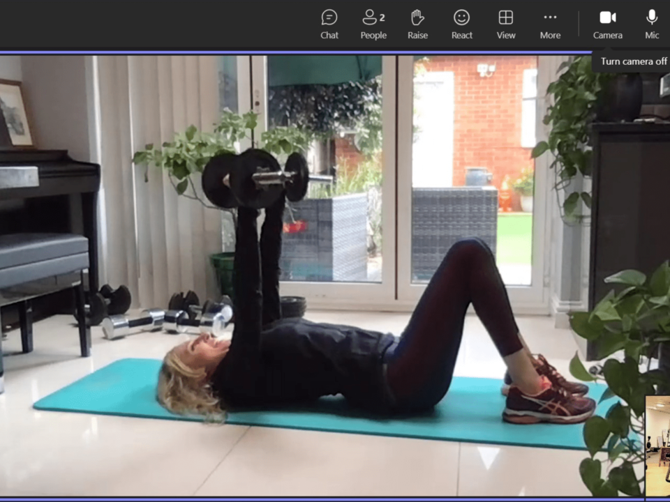 A screenshot of a video call where a client is performing a chest press exercise and has hire a personal trainer to work with her for motivation, knowledege, and accountability